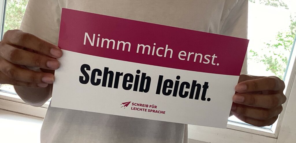 Jemand hält ein Schild mit der Aufschrift: Nimm mich ernst. Schreib leicht.