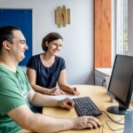 Kathrin Usenko mit einem Teilnehmer am Computer Ein Mann und Kathrin Usenko schauen auf einen Bildschirm