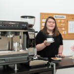 Alexandra Herzog reicht eine Tasse Kaffee über die Theke